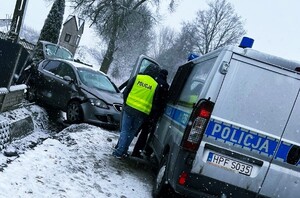 policyjny radiowóz, policjanci stoją przy radiowozie, w ogrodzeniu rozbity samochód