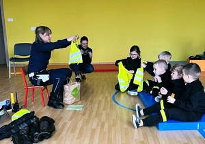 policjantka ruchu drogowego rozmawia z dziećmi o odblaskach prezentując im kamizelkę odblaskową