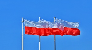 trzy flagi biało-czerwone na masztach w tle błękitne niebo
