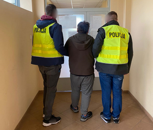 policjanci w kamizelkach odblaskowych z napisem POLICJA prowadzą pomiędzy sobą zatrzymanego mężczyznę