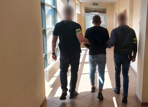 nieumundurowani policjanci z opasakmi na przedramionach z napisem POLICJA prowadzą zatrzymanego mężczyznę