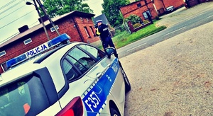 policjant ruchu drogowego stojąc przed radiowozem dokonuje pomiaru prędkości ręcznym miernikiem laserowym