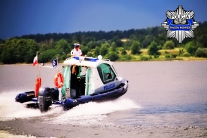 policyjna łódź motorowa płynie z dużą prędkością. widoczna rozbryzgująca się woda i policjant w białej czapce. zachmurzone niebo a w górnym prawym narożniku grafika policyjna gwiazda z napisem POLICJA Tomaszów Mazowiecki