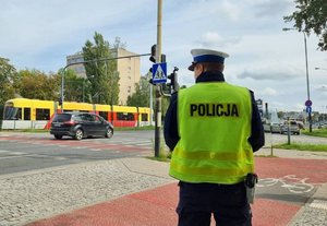 policjant ruchu drogowego stoi w rejonie skrzyżowania, widoczne znaki, sygnalizacja świetlna , jezdnia i  ścieżka rowerowa
