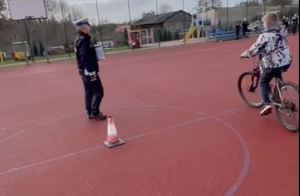 policjant ruchu drogowego nadzoruje poprawność wykonywanych zdań przez nastolatka jadącego na rowerze - egzamin na kartę rowerową