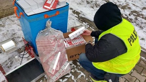 Policjant kuca przy paczkach papierosów.