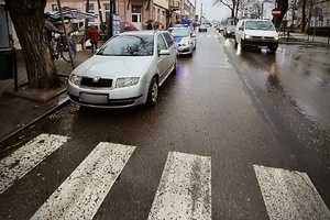 policyjny radiowóz z włączonym sygnalizatorem świetlnym stoi za autem zaparkowanym tuż przed przejściem dla pieszych