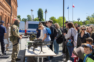 Kontrterrorysta stoi przy stole na którym wystawiony jest sprzęt policyjny, przed stoiskiem stoją ludzie.