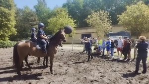 zdjęcie przedstawiające wizytę dzieci na terenie ogniwa konnego. widoczne dzieci i policyjni jeźdźcy na koniach w trakcie ćwiczeń