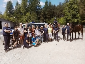 zdjęcie przedstawiające wizytę dzieci na terenie ogniwa konnego. widoczne dzieci i policyjni jeźdźcy na koniach w trakcie ćwiczeń