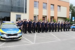 umundurowani policjanci oddają honory stojąc przezd budynkiem komendy i koło radiowozu z włączoną sygnalizacją świetlną