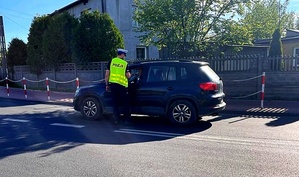 policjant ruchu drogowego stojąc przy drzwiach kierowcy zatrzymanego do kontroli pojazdu wykonuje badanie trzeźwości osoby kierującej