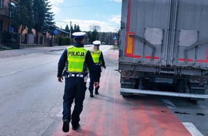 policjanci ruchu drogowego w kamizelkach odblaskowych idą wzdłuż skrzyni ładunkowej pojazdu ciężarowego do kabiny auta