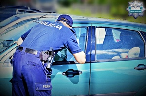 policjant zagląda przez szybę do wnętrza samochodu stojącego w słońcu