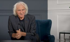 Aktor Jerzy Kryszak siedzi na fotelu i patrzy w obiektyw przed sobą