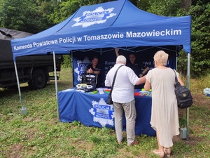 policjanci na stoisku profilaktycznym pod namiotem prezentują zainteresowanym policyjne wyposażenie służbowe oraz przekazują ulotki profilaktyczne i odblaskowe gadżety