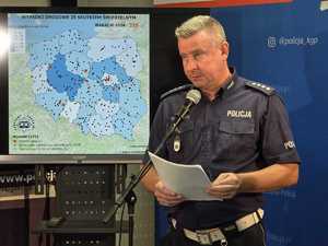 policjant ruchu drogowego stoi przed mikrofonem w tle widoczna mapa wypadków drogowych