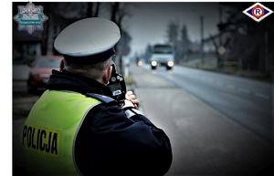 policjant ruchu drogowego mierzy prędkość nadjeżdżających pojazdów laserowym miernikiem prędkość. w oddali nadjeżdżający pojazd.