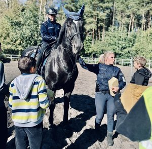 policjanta siedzi na koniu, obok stoi druga policjantka, na pierwszym planie stoi tyłem chłopiec biorący udział w pokazie konnym