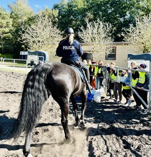 policjantka w trakcie jazdy konnej, na drugim planie dzieci obserwujące wybieg