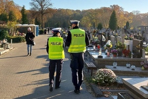 policjanci idą cmentarną alejką.