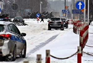 Pojazdy i radiowóz jadące po ośnieżonej drodze.