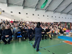 Umundurowana policjantka prowadzi spotkanie z liczną grupą dzieci i młodzieży.