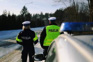 Dach radiowozu, w tle policjant i policjantka z ruchu drogowego.