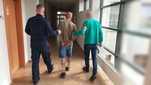 Policjanci prowadzą korytarzem zatrzymanego mężczyznę.