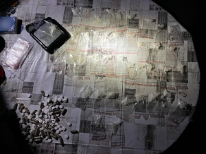 Białe kryształki w foliowych torebkach, tabletki i waga na blacie stołu.