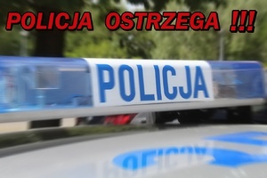 Sygnalizator świetlny na dachu policyjnego radiowozu. Rozmyte tło i napis powyżej o treść Policja Ostrzega!