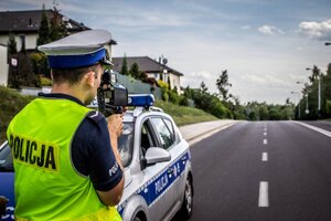 Policjant ruchu drogowego mierzy prędkość stojąc przy radiowozie.