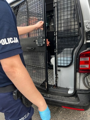Policjant zamyka zakratowane pomieszczenie w radiowozie policyjnym , w którym siedzi zatrzymany mężczyzna.