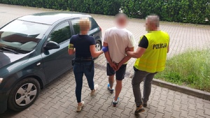 Policjantka i policjant prowadzą zatrzymanego mężczyznę do samochodu.