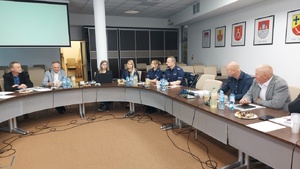 Uczestnicy spotkania w tym umundurowana policjantka i policjant siedzą przy stołach ustawionych w owal.