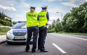 Policjanci ruchu drogowego stoją tyłem przy drodze przed nimi radiowóz.