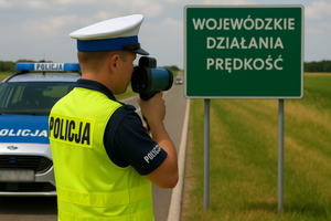 Policjant mierzący prędkość pojazdu, obok radiowóz i tabliczka z napisem wojewódzkie działania prędkość.