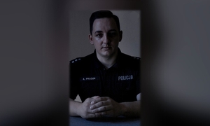Policjant siedzi przy biurku w zaciemnionym pomieszczeniu.
