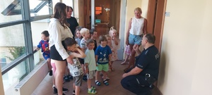Dzieci wraz z opiekunkami i policjantem, zwiedzają komendę, i oglądają radiowóz.