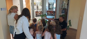 Dzieci wraz z opiekunkami i policjantem, zwiedzają komendę, i oglądają radiowóz.
