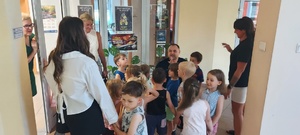 Dzieci wraz z opiekunkami i policjantem, zwiedzają komendę, i oglądają radiowóz.