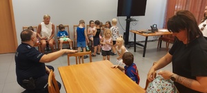 Dzieci wraz z opiekunkami i policjantem, zwiedzają komendę, i oglądają radiowóz.
