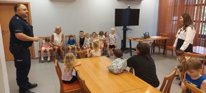 Dzieci wraz z opiekunkami i policjantem, zwiedzają komendę, i oglądają radiowóz.