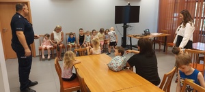 Dzieci wraz z opiekunkami i policjantem, zwiedzają komendę, i oglądają radiowóz.