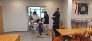 Dzieci wraz z opiekunkami i policjantem, zwiedzają komendę, i oglądają radiowóz.