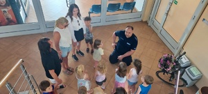 Dzieci wraz z opiekunkami i policjantem, zwiedzają komendę, i oglądają radiowóz.