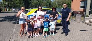 Dzieci wraz z opiekunkami i policjantem, zwiedzają komendę, i oglądają radiowóz.