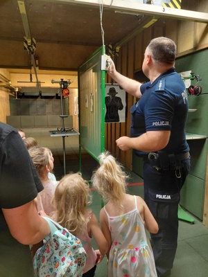 Dzieci wraz z opiekunkami i policjantem, zwiedzają komendę, i oglądają radiowóz.