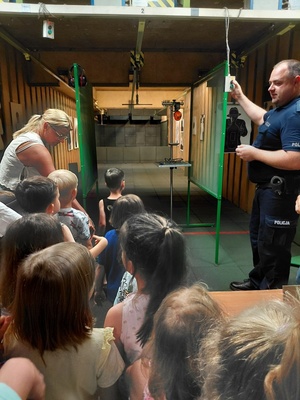 Dzieci wraz z opiekunkami i policjantem, zwiedzają komendę, i oglądają radiowóz.