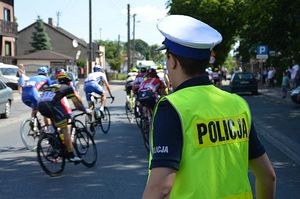 Policjant ruchu drogowego zabezpiecza przejazd wyścigu kolarskiego, w tle widoczni kolarze.
